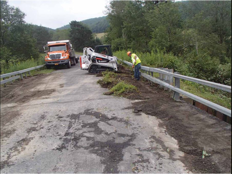 Bridge maintenance crew removing soil and vegetation from bridge deck.
