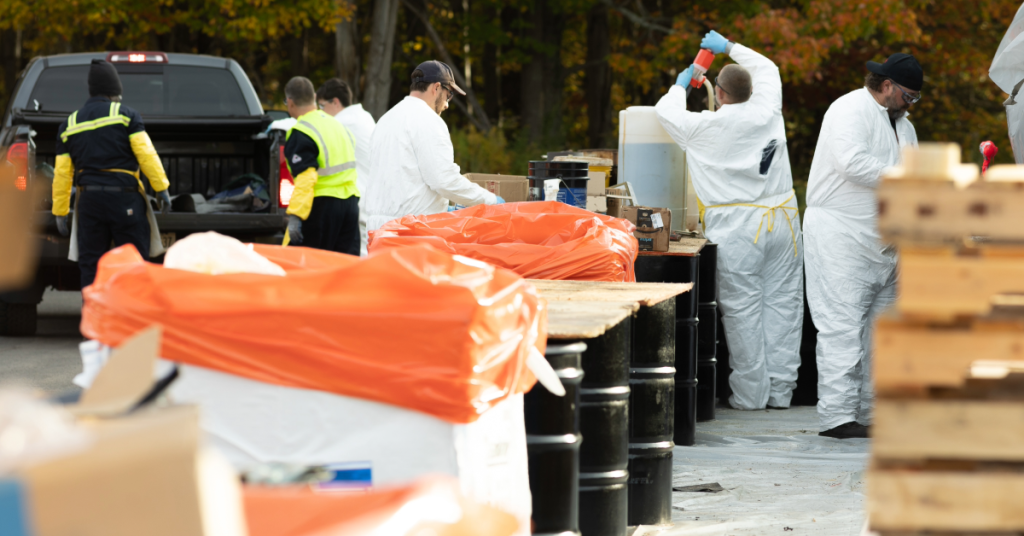 Individuals wearing protective gear separate clean sweep collections into barrels lined with orange bags.